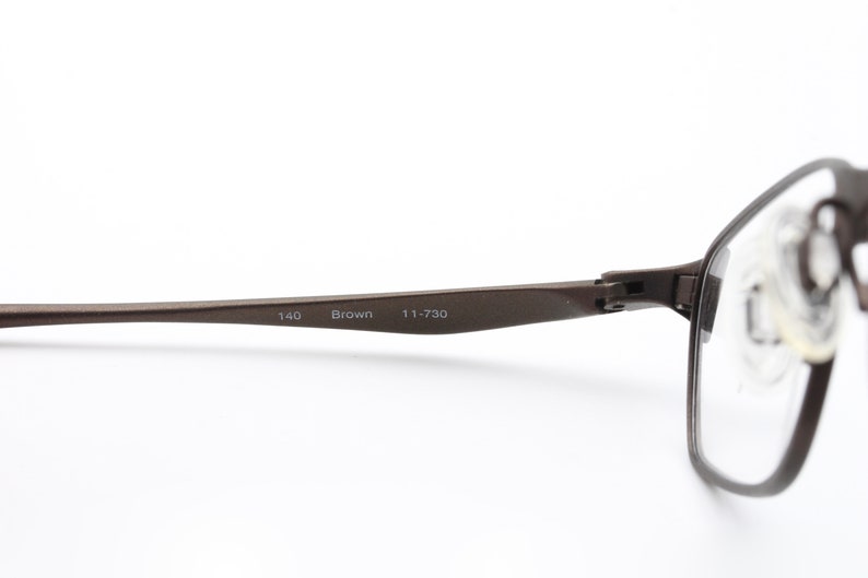 May include: Brown metal frame eyeglasses with clear lenses. The frame has the text "140 Brown 111-730" printed on the side.
