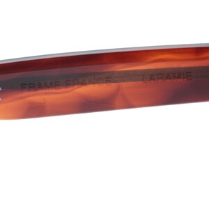 May include: Close-up of the inside of a tortoiseshell-coloured sunglasses frame. The frame is marked with "CE", "FRAME FRANCE", and "LARAMIE".