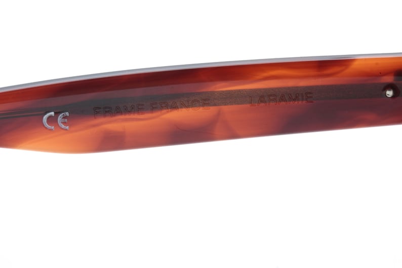 May include: Close-up of the inside of a tortoiseshell-coloured sunglasses frame. The frame is marked with "CE", "FRAME FRANCE", and "LARAMIE".
