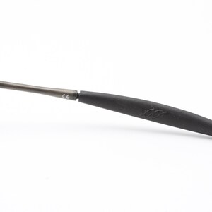 May include: A close-up of a black and gray temple tip for eyeglasses. The tip is made of a soft, flexible material and has a small logo on it.