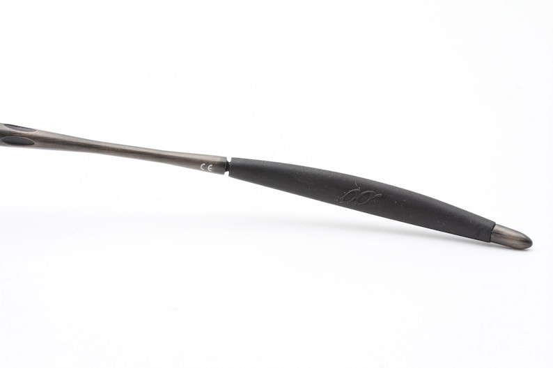 May include: A close-up of a black and gray temple tip for eyeglasses. The tip is made of a soft, flexible material and has a small logo on it.