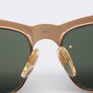 May include: Close-up of a pair of gold-tone sunglasses with green lenses. The sunglasses have a metal frame and are marked with the number "55" on the bridge.
