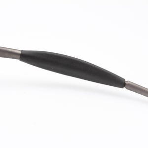 May include: Close-up of a portion of a pair of eyeglasses. The frame is a dark gray metal with a black rubber grip. The text "IN U.S.A." is visible on the frame.