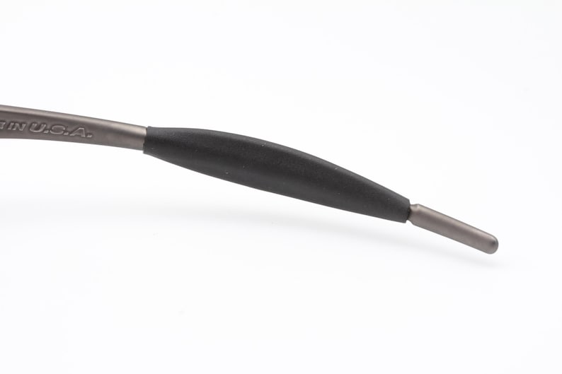 May include: Close-up of a portion of a pair of eyeglasses. The frame is a dark gray metal with a black rubber grip. The text "IN U.S.A." is visible on the frame.
