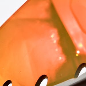 May include: Close-up of a bright orange and yellow plastic object with a series of small holes along the bottom edge. The object is translucent and has a slight shimmer.