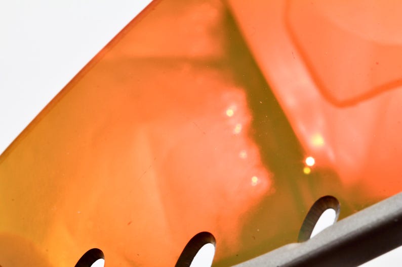 May include: Close-up of a bright orange and yellow plastic object with a series of small holes along the bottom edge. The object is translucent and has a slight shimmer.