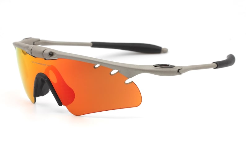 May include: A pair of gray wraparound sunglasses with orange lenses. The sunglasses have a sporty design and are made of a durable material.