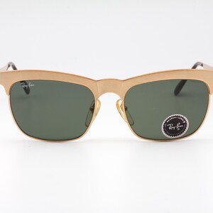 May include: Gold-tone Ray-Ban sunglasses with green lenses. The sunglasses have a classic aviator style with a thin metal frame.