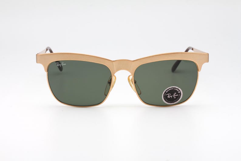 May include: Gold-tone Ray-Ban sunglasses with green lenses. The sunglasses have a classic aviator style with a thin metal frame.