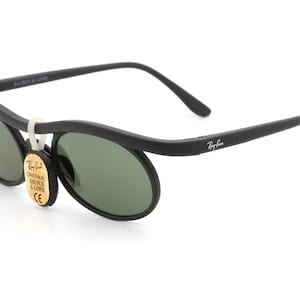 May include: Black Ray-Ban sunglasses with green lenses and a curved frame. The sunglasses have a tag that reads "Original Bausch & Lomb CE".