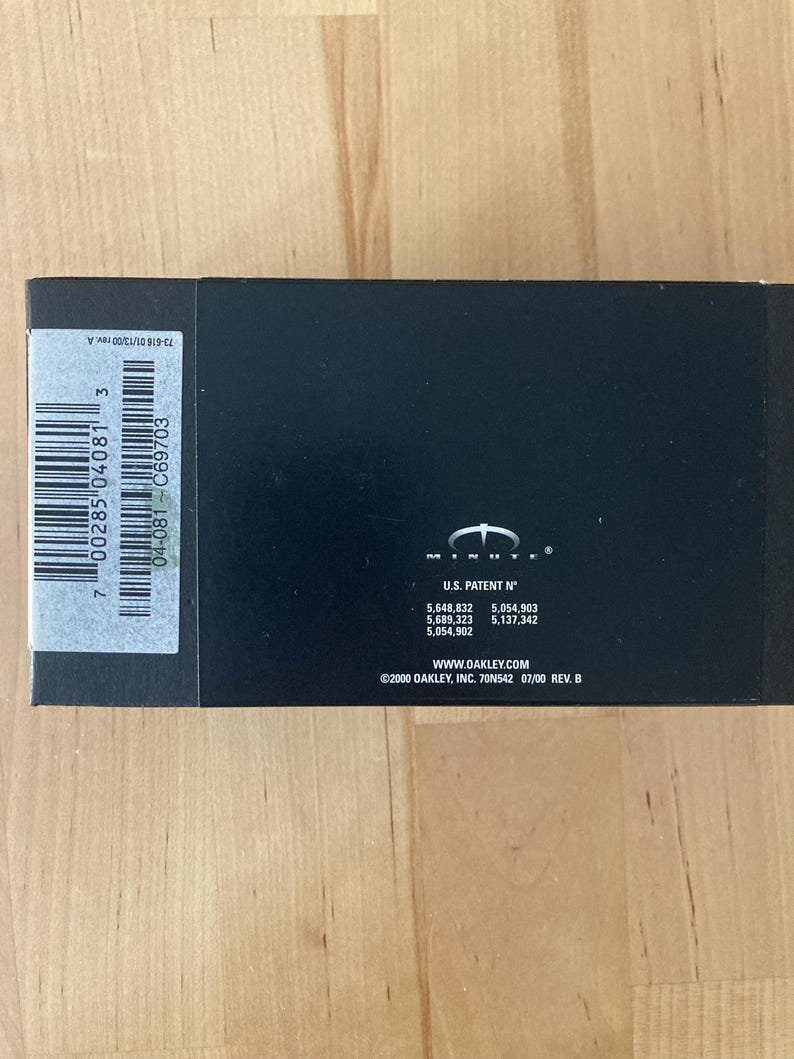 May include: A black rectangular box with a white barcode label and the text "7 00285 04081 3". The box also features the Oakley logo and patent numbers. The text "WWW.OAKLEY.COM" is visible.