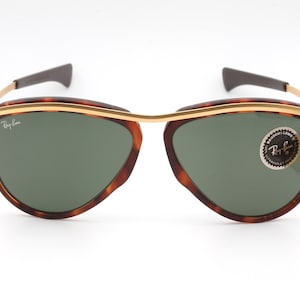 Pu&ograve; includere: Occhiali da sole con montatura tartaruga, dettagli dorati e lenti verdi. Gli occhiali hanno il logo Ray-Ban sulla lente sinistra e un adesivo Ray-Ban sulla lente destra.