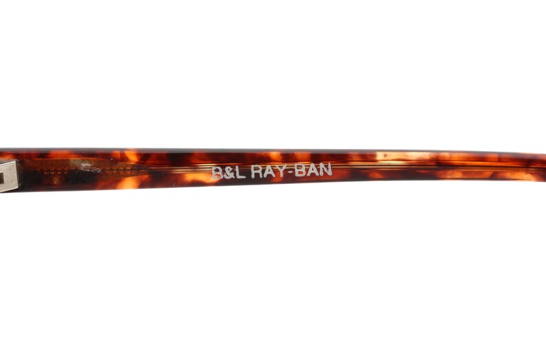 May include: Close-up of the arm of a pair of tortoiseshell sunglasses with the text "B&L RAY-BAN" printed on the arm.