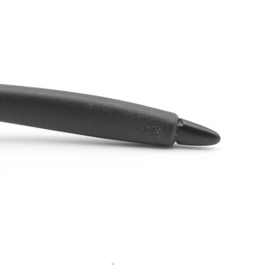 May include: Close-up of a black eyeglass arm with a rounded, textured grip and a pointed tip. The arm curves slightly, and the tip has a small marking. The background is plain white.