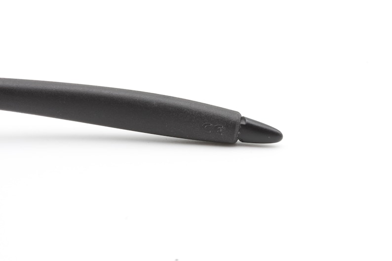 May include: Close-up of a black eyeglass arm with a rounded, textured grip and a pointed tip. The arm curves slightly, and the tip has a small marking. The background is plain white.