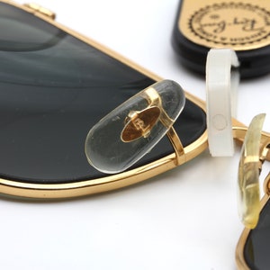 Puede incluir: Gafas de sol de metal dorado con lentes negros y patillas de pl&aacute;stico transparente. Las patillas tienen el logotipo de Ray-Ban.