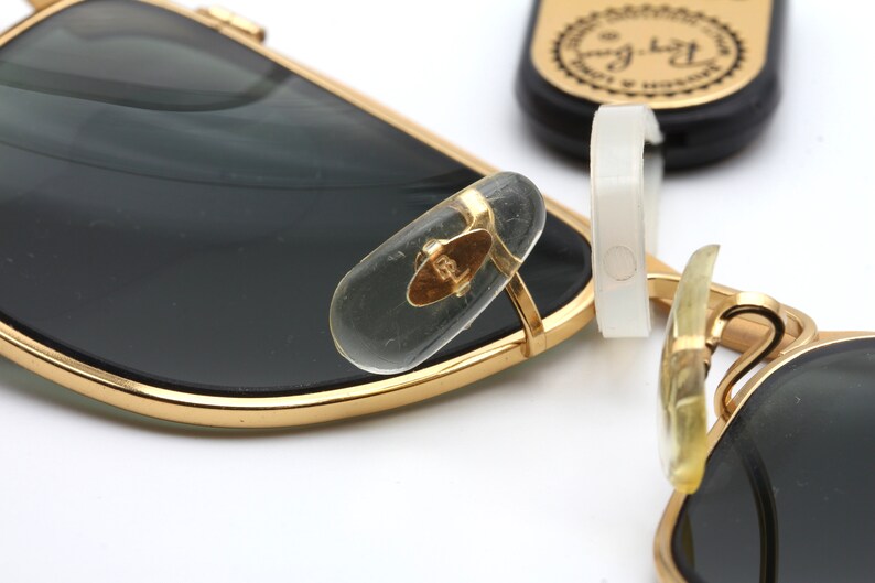 Puede incluir: Gafas de sol de metal dorado con lentes negros y patillas de pl&aacute;stico transparente. Las patillas tienen el logotipo de Ray-Ban.