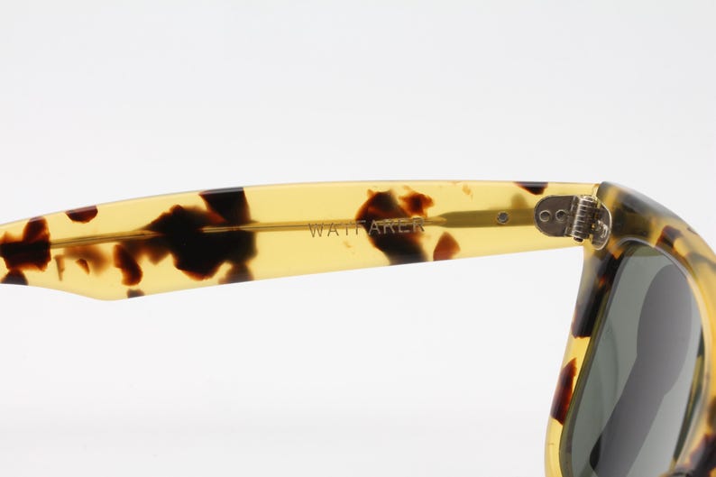 Puede incluir: Primer plano de gafas de sol con estampado de carey. La patilla de las gafas de sol es de color amarillo transl&uacute;cido con manchas marrones oscuras. La palabra "WATTAKER" est&aacute; impresa en la patilla.