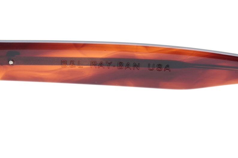 May include: Close-up of the brown tortoiseshell frame of a pair of Ray-Ban sunglasses. The text "B&L RAY-BAN USA" is engraved on the frame.