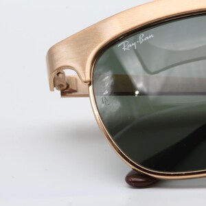 May include: Gold-tone Ray-Ban sunglasses with green lenses. The sunglasses have a classic aviator style with a thin metal frame.