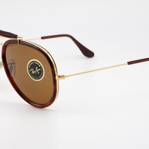 May include: Aviator-style sunglasses with brown lenses and a gold frame. The frames have a tortoiseshell pattern on the top and sides. The Ray-Ban logo is visible on the lens.