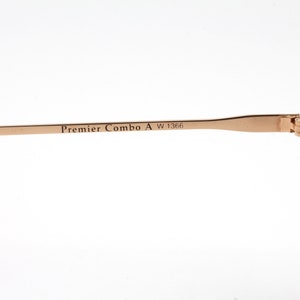 Op de afbeelding: Close-up van de gouden metalen poot van een paar schildpadzonnebrillen. De poot is gegraveerd met de tekst "Premier Combo A W 1366".