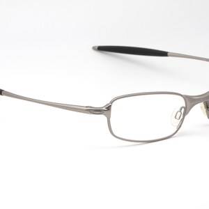 May include: A pair of eyeglasses with a silver metal frame and rectangular lenses. The temples have black rubberized tips. The glasses are set against a white background.