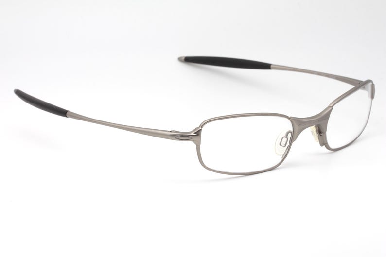 May include: A pair of eyeglasses with a silver metal frame and rectangular lenses. The temples have black rubberized tips. The glasses are set against a white background.