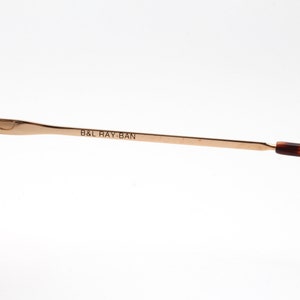 Op de afbeelding: Close-up van de gouden metalen armen van een paar schildpadzonnebrillen. De zonnebrillen zijn gemarkeerd met "B&L RAY-BAN".