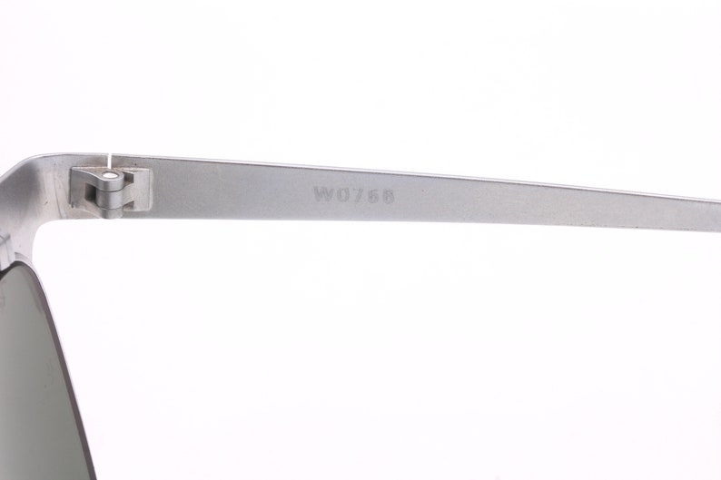 May include: Close-up of the silver metal arm of a pair of sunglasses. The arm is engraved with the number "W0768".
