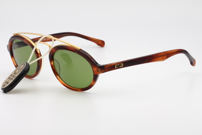 May include: Brown tortoise shell sunglasses with gold accents and green lenses. The sunglasses have a round shape and a thin gold metal bridge. The brand name is visible on the right temple.
