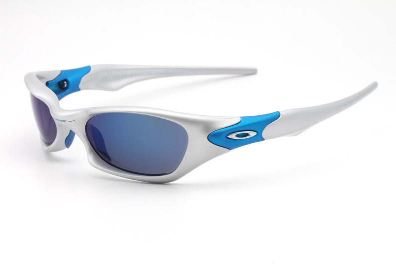 May include: Silver and blue sunglasses with a blue accent on the side. The lenses are a dark blue color.