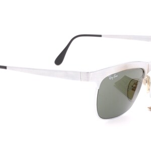 May include: Silver-framed sunglasses with green lenses. The sunglasses have a Ray-Ban logo on the side.