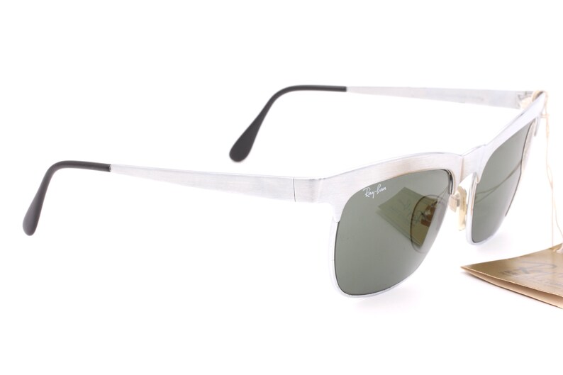 May include: Silver-framed sunglasses with green lenses. The sunglasses have a Ray-Ban logo on the side.