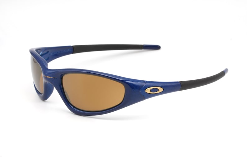 May include: Blue and black sunglasses with brown lenses. The sunglasses have a gold logo on the side.