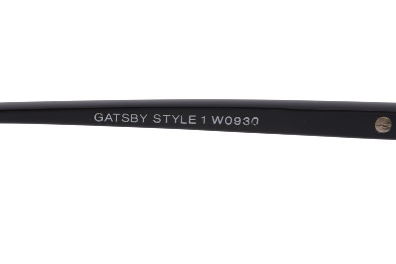 May include: Close-up of the black arm of a pair of glasses with the text "GATSBY STYLE 1 W0930" printed on it.