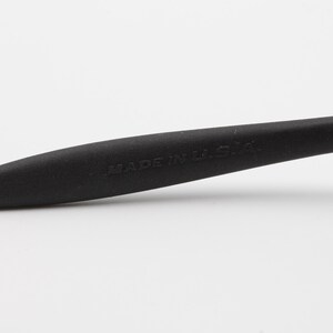 May include: Close-up of a black rubber temple tip for a pair of glasses. The temple tip has the words "MADE IN USA" printed on it.