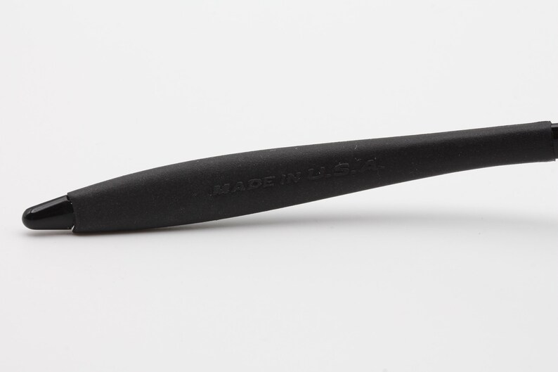 May include: Close-up of a black rubber temple tip for a pair of glasses. The temple tip has the words "MADE IN USA" printed on it.