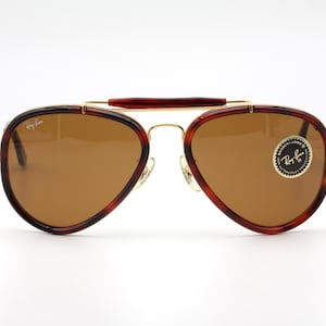 May include: Aviator-style sunglasses with brown lenses and a gold-tone metal frame. The frames have a tortoiseshell pattern on the edges and a brown bridge. The Ray-Ban logo is visible on the lens.