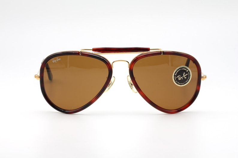 May include: Aviator-style sunglasses with brown lenses and a gold-tone metal frame. The frames have a tortoiseshell pattern on the edges and a brown bridge. The Ray-Ban logo is visible on the lens.
