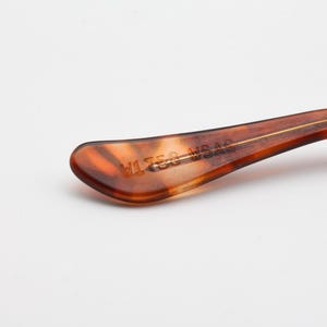 May include: Close-up of a brown and amber-colored eyeglass arm. The arm has a curved shape with a gold-colored stripe running down the center. The text "V1758 WSAS" is printed on the arm.