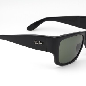 May include: Black sunglasses with a rectangular frame and green-tinted lenses. The Ray-Ban logo is visible on the left arm. The sunglasses have a sleek, modern design.