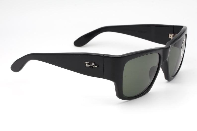 May include: Black sunglasses with a rectangular frame and green-tinted lenses. The Ray-Ban logo is visible on the left arm. The sunglasses have a sleek, modern design.