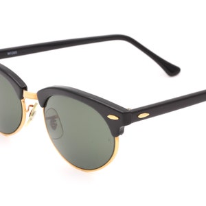 May include: Black sunglasses with gold accents and green lenses. The sunglasses have a classic, rounded shape.