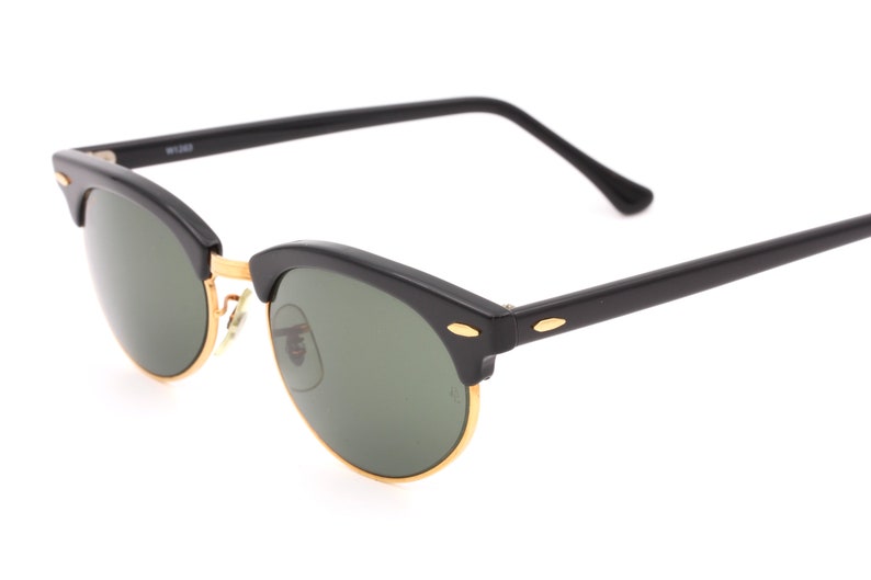 May include: Black sunglasses with gold accents and green lenses. The sunglasses have a classic, rounded shape.