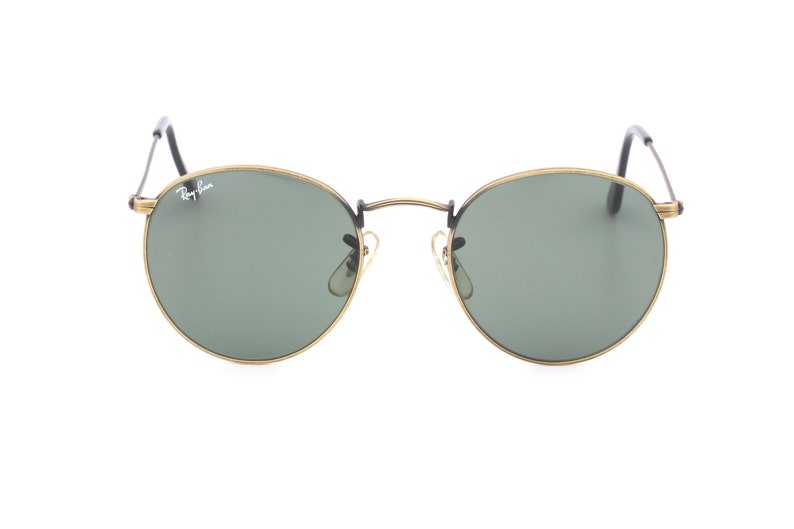 Puede incluir: Gafas de sol redondas con montura dorada y lentes verdes. El logotipo de Ray-Ban es visible en la lente derecha.