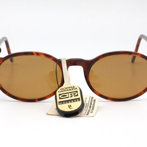 May include: Brown tortoise shell round sunglasses with brown lenses. The sunglasses have gold accents on the temples and a small tag attached to the left temple that says "Ray-Ban".
