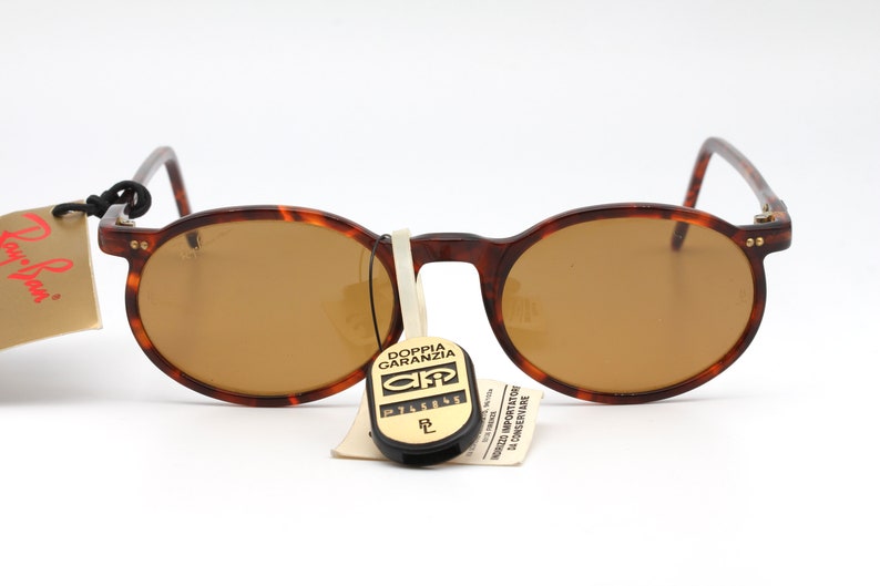 May include: Brown tortoise shell round sunglasses with brown lenses. The sunglasses have gold accents on the temples and a small tag attached to the left temple that says "Ray-Ban".