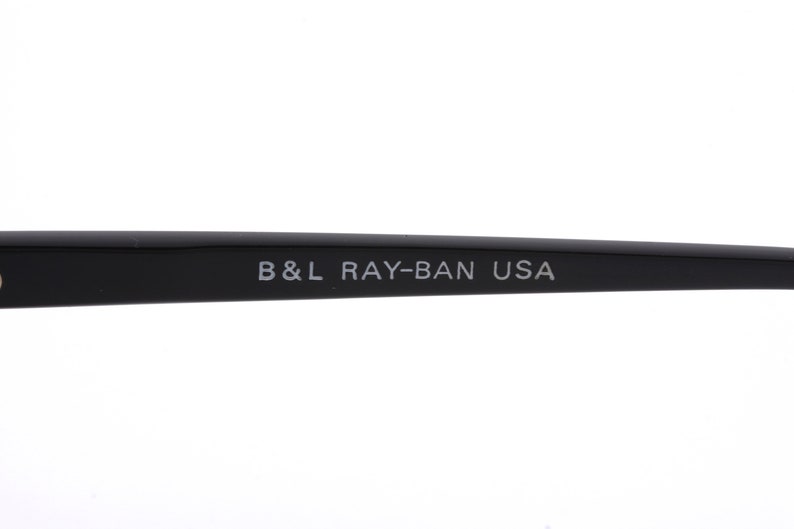 May include: Close-up of the black arm of a pair of Ray-Ban sunglasses with the text "B&L RAY-BAN USA" printed in white.