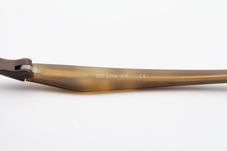 May include: Close-up of a portion of eyeglasses. The frame arm is a light brown color with the text "Off Line 4.0" and "CE" printed on the arm. The frame is made of a light brown material.
